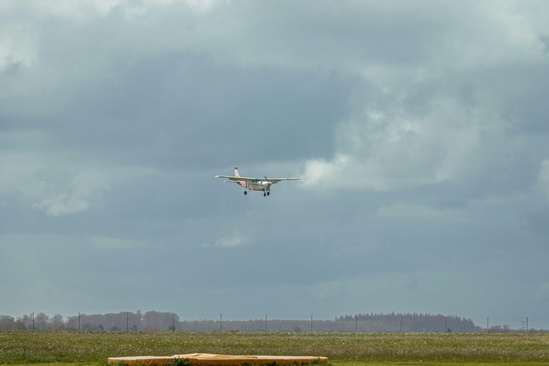 A plane flying over a field with a bench in the foreground