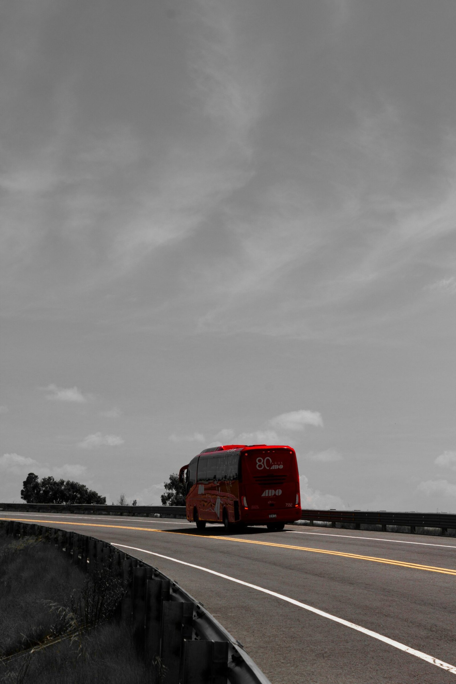 A red bus driving down a highway under a cloudy sky